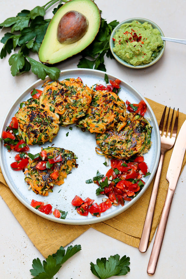 Bunter Teller mit knusprigen Gemüserösti aus Süßkartoffel, Pastinake und Zucchini, serviert mit frischer Tomatensalsa und cremiger Guacamole, dekoriert mit frischer Petersilie und einer Avocado.